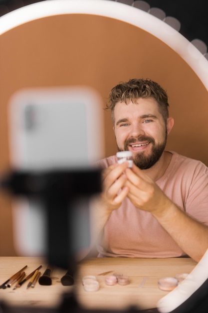 Hombre vlogueando sobre maquillaje y productos de belleza Hombre filmando un tutorial de maquillaje Un chico enseñando un tutorial de maquillaje usando la diversidad de su teléfono y el concepto de blogger