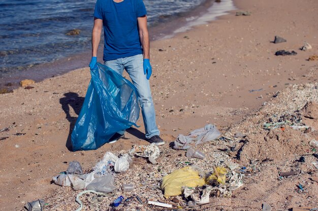 Hombre voluntario con bolsa grande para basura recogiendo basura en la playa. Concepto de contaminación ambiental