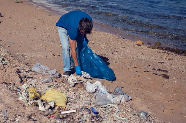 Hombre voluntario con bolsa grande para basura recogiendo basura en la playa. Concepto de contaminación ambiental