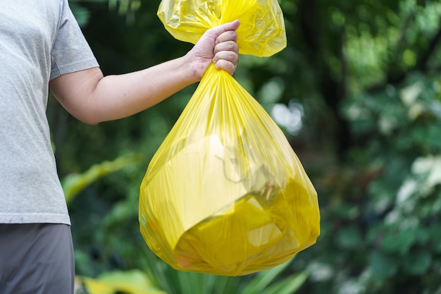 Hombre voluntario de caridad sosteniendo una bolsa amarilla de basura y una botella de plástico para reciclar la limpieza