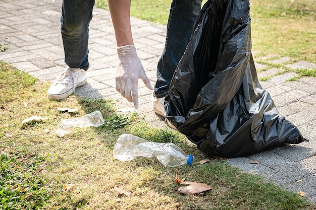 Foto hombre voluntario con guantes caminando y deteniéndose para recolectar botellas de plástico en una bolsa negra de plástico para limpiar el parque durante la actividad ambiental para recolectar basura