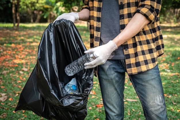 Hombre voluntario en guantes para recoger una botella de plástico en una bolsa negra de plástico para limpiar el parque durante la actividad ambiental para recolectar basura