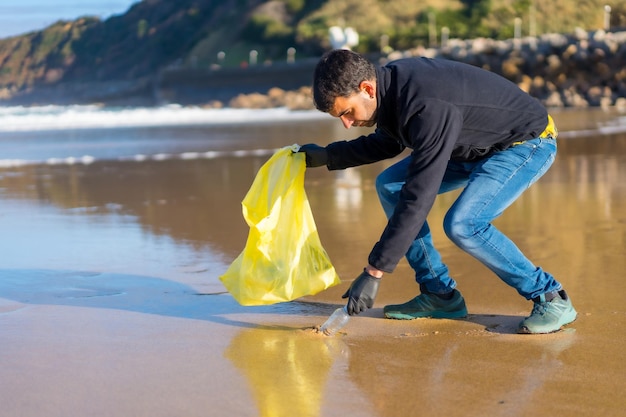 Hombre voluntario recogiendo basura o plástico en el concepto de ecología de la playa