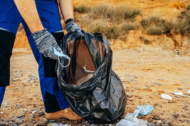 Hombre voluntario recogiendo máscaras médicas usadas en la playa cerca del océano