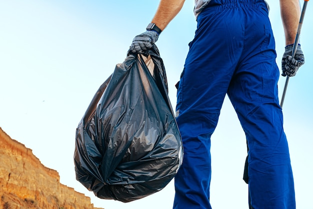 Hombre voluntario en uniforn recogiendo basura en la playa con un extensor de alcance