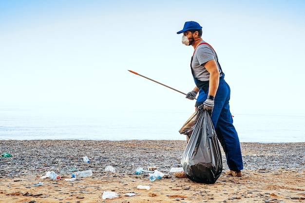 Hombre voluntario en uniforn recogiendo basura en la playa con un extensor de alcance