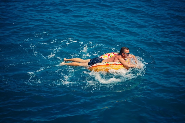 Un hombre yace en un gran círculo de goma inflable y flota en el mar azul en un día soleado de verano