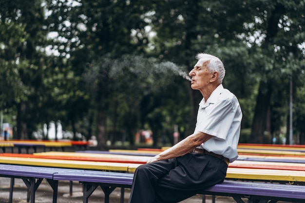 Los hombres adultos mayores que fuman cigarrillos al aire libre en el parque de la ciudad cuando están sentados en el banco.