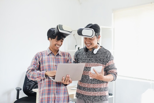 Hombres asiáticos que usan gafas VR en la cabeza mientras trabajan en una computadora portátil y una tableta