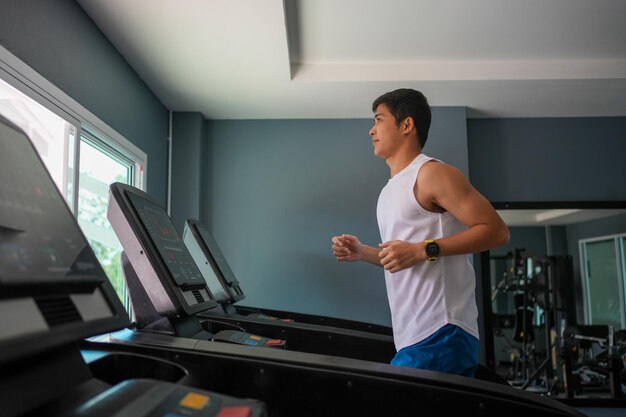 Los hombres asiáticos son felices trotando y corriendo en una caminadora en el gimnasio