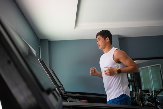 Los hombres asiáticos son felices trotando y corriendo en una caminadora en el gimnasio