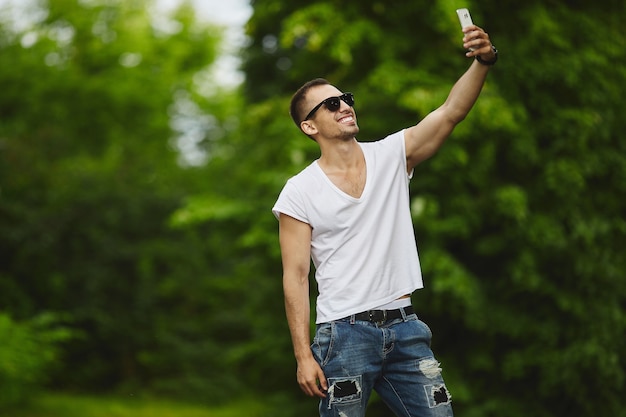 Hombres atléticos jóvenes guapos con estilo, con camiseta blanca y jeans, hacen un selfie en su teléfono inteligente