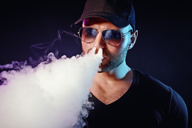 Hombres con barba en gafas de sol vaping y liberan una nube de vapor