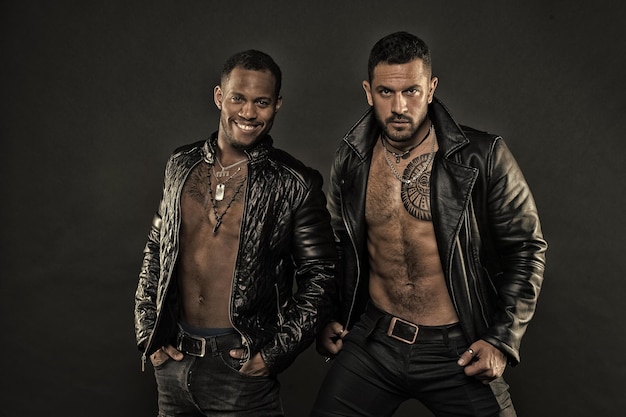 Hombres en caras sonrientes con cerdas y tatuajes Concepto de moda y estilo Los machos con torsos musculosos se ven atractivos en chaquetas de cuero de fondo oscuro Los hombres con torsos musculosos sexy se ven brutalmente