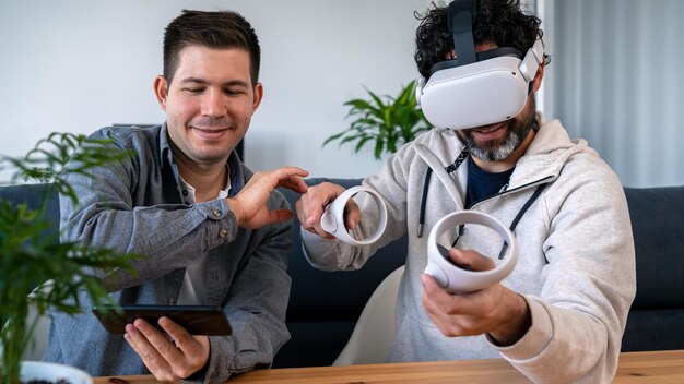 Hombres caucásicos disfrutando de gafas de realidad virtual mientras se sientan a la mesa en casa