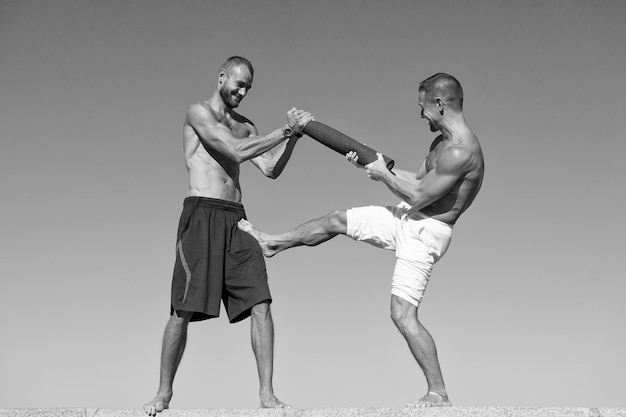 Hombres con colchoneta de yoga capturada en movimiento fondo de cielo azul Deportista luchando Practicar habilidades de lucha al aire libre Mejorar habilidades de lucha Hombres torsos musculosos desnudos luchando Concepto de entrenador experimentado