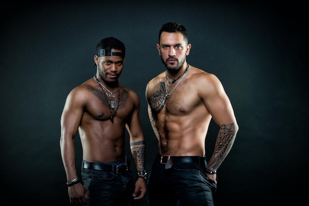 Hombres con cuerpos sexys en forma Hombre africano con una sonrisa encantadora con gorra de béisbol Deportistas con pechos y brazos tatuados aislados en el concepto de cuidado corporal de fondo negro Atletas preparándose para el concurso