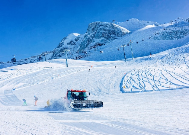 Hombres esquiadores y practicantes de snowboard en el glaciar Hintertux en Tirol en Mayrhofen, Alpes invernales. Personas con esquí y snowboard en Hintertuxer Gletscher en montañas alpinas. Ratrack Snowcat trabajando