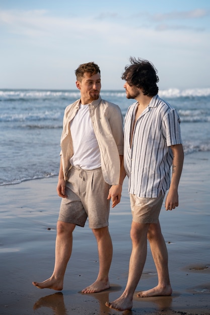 Hombres gay de tiro completo tomados de la mano en la playa