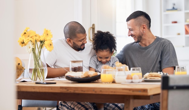 Los hombres gays y la familia sonríen juntos en el desayuno en el comedor de su casa moderna, un vínculo feliz y una niña come una comida saludable para el almuerzo o el brunch con sus padres LGBTQ en casa.