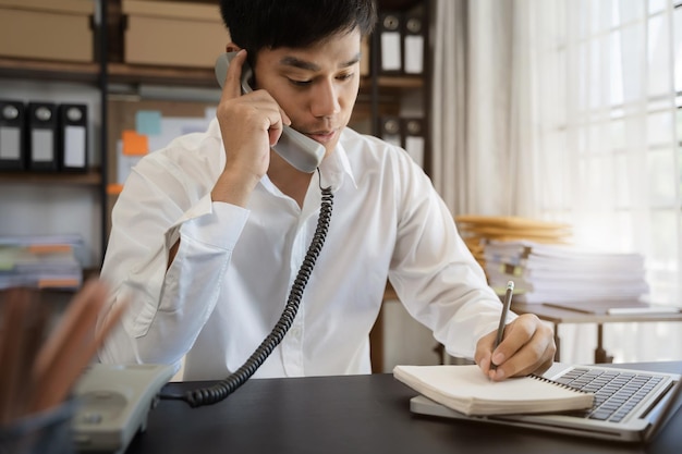 Los hombres hablan por teléfono móvil y toman notas en sus cuadernos mientras trabajan en computadoras portátiles, trabajo de negocios en línea desde el concepto de teletrabajo en el hogar