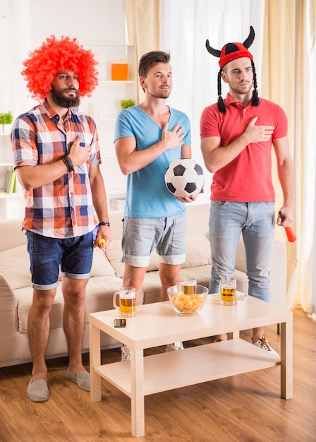 Los hombres jóvenes beben cerveza, comen pizza y animan al fútbol