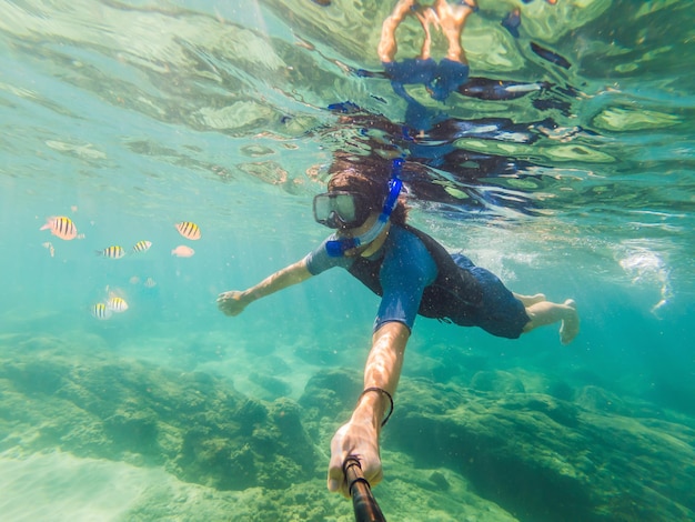 Hombres jóvenes buceando explorando el fondo del paisaje de arrecifes de coral submarinos en el océano azul profundo con peces coloridos y vida marina