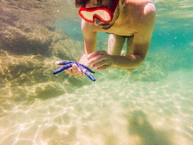 Hombres jóvenes buceando explorando el fondo del paisaje de arrecifes de coral submarinos en el océano azul profundo con peces coloridos y vida marina