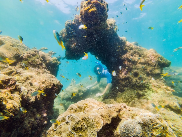 Hombres jóvenes buceando explorando el fondo del paisaje de arrecifes de coral submarinos en el océano azul profundo con peces coloridos y vida marina