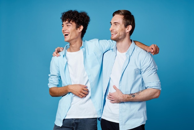 Hombres jóvenes con camisas idénticas abrazándose en un fondo azul mejores amigos divertidos foto de alta calidad