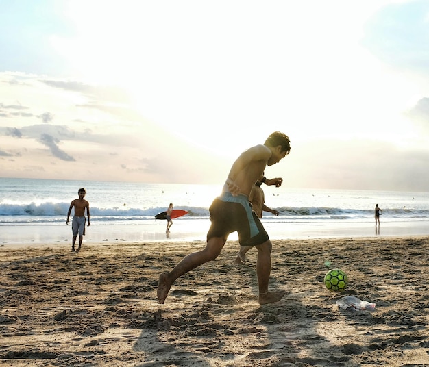 Foto hombres jóvenes jugando al fútbol en la arena en la playa contra el cielo durante la puesta de sol