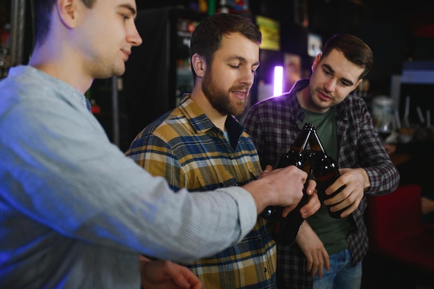 Hombres jóvenes con ropa informal hablan riéndose y bebiendo mientras están sentados en el mostrador del bar en el pub