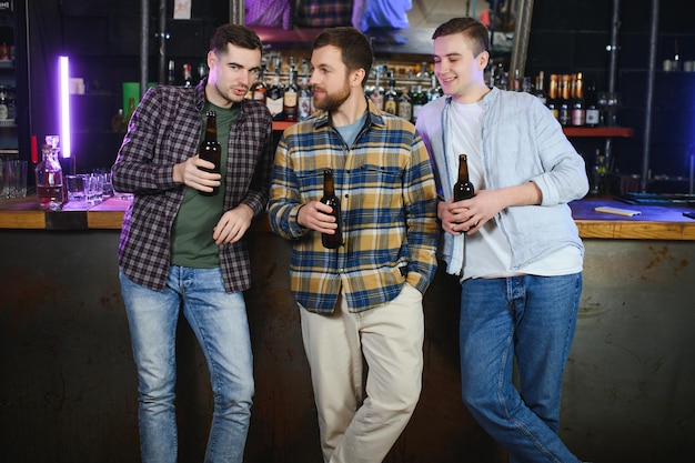 Hombres jóvenes con ropa informal hablan riéndose y bebiendo mientras están sentados en el mostrador del bar en el pub