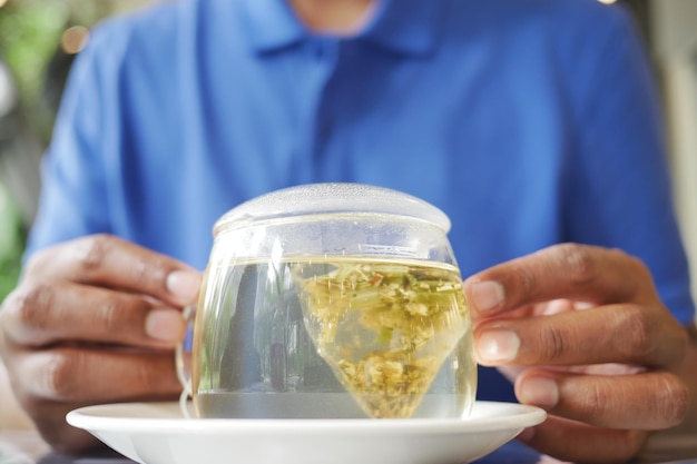 Hombres jóvenes sosteniendo una taza de té verde y una bolsita de té en la mesa