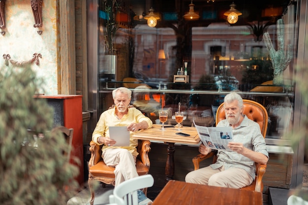 Hombres jubilados. Dos hombres jubilados de pelo gris sentados fuera de la cafetería y leyendo