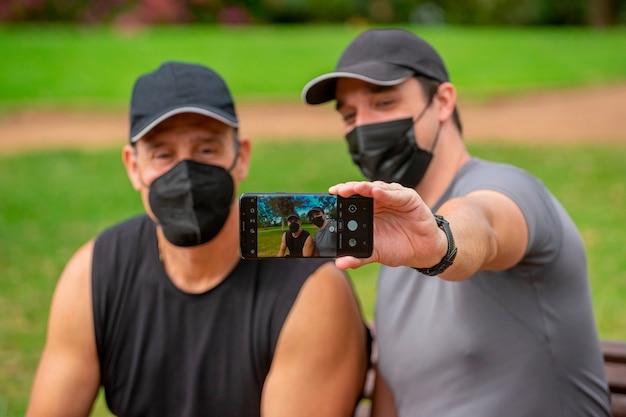 Hombres con máscaras en el parque haciendo deporte y tomando un selfie con un teléfono inteligente