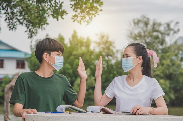 Hombres y mujeres asiáticos de regreso a la escuela con una mascarilla y un apretón de manos mantener el distanciamiento social normal sin tocar