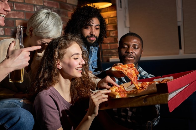 Hombres y mujeres comiendo pizza y viendo la televisión.Fiesta en casa.Concepto de comida rápida. Los estadounidenses pasan tiempo libre juntos por la noche.