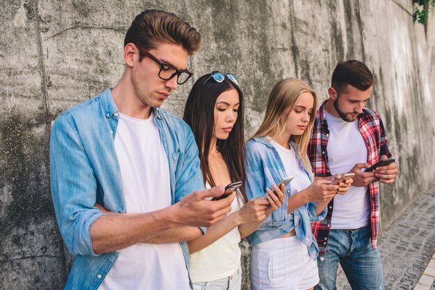 Hombres y mujeres jóvenes están de pie y usan teléfonos inteligentes