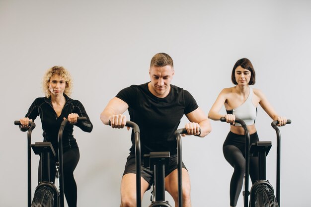 Hombres y mujeres jóvenes que usan bicicleta de aire para hacer ejercicio cardiovascular en el gimnasio de entrenamiento cruzado