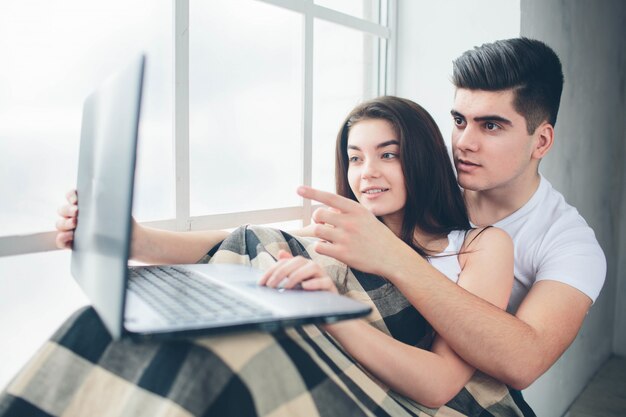 Hombres y mujeres jóvenes trabajan en la computadora o buscan información en Internet en una ventana inundada de luz solar