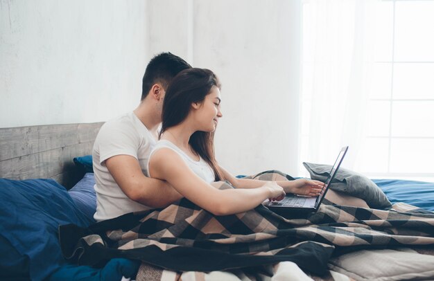 Hombres y mujeres jóvenes trabajan en la computadora o buscan información sobre el Interneton la cama.