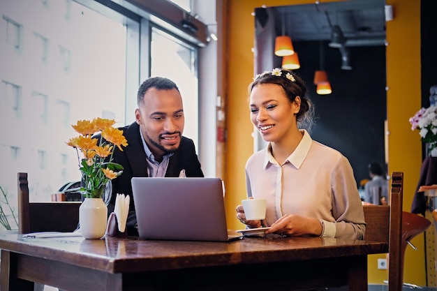 Hombres y mujeres de negocios afroamericanos negros beben café y usan una computadora portátil en un restaurante.