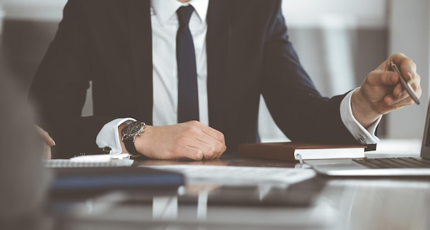 Hombres y mujeres de negocios desconocidos sentados usando una computadora portátil y discutiendo preguntas en una reunión en el primer plano de la oficina moderna