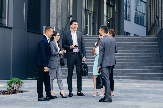 Hombres y mujeres de negocios discuten negocios. Grupo de seis jóvenes empresarios caucásicos hombres y mujeres reunidos discutiendo fuera del edificio de oficinas.