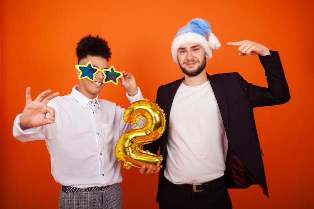 Hombres multiculturales divertidos con un sombrero de Navidad y grandes gafas de estrellas que muestran los me gusta y el signo de ok