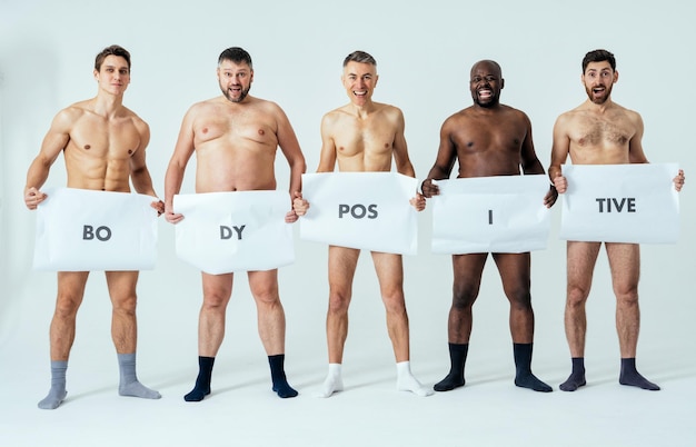 Foto hombres multiétnicos posando para un conjunto de belleza positiva corporal de edición masculina que muestra mensajes en pancartas. chicos sin camisa con diferentes edades y cuerpo usando ropa interior de boxeadores
