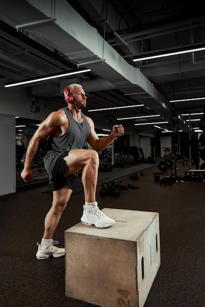 Hombres musculosos sexy usando la plataforma para sus piernas sobre un fondo de colores oscuros de gimnasio.