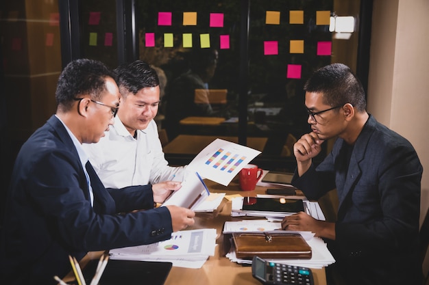 Hombres de negocios asiáticos que discuten el trabajo que se sienta en sala de conferencias de la oficina en la escena de la noche