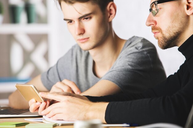 Hombres de negocios atractivos que usan teléfonos inteligentes en el lugar de trabajo